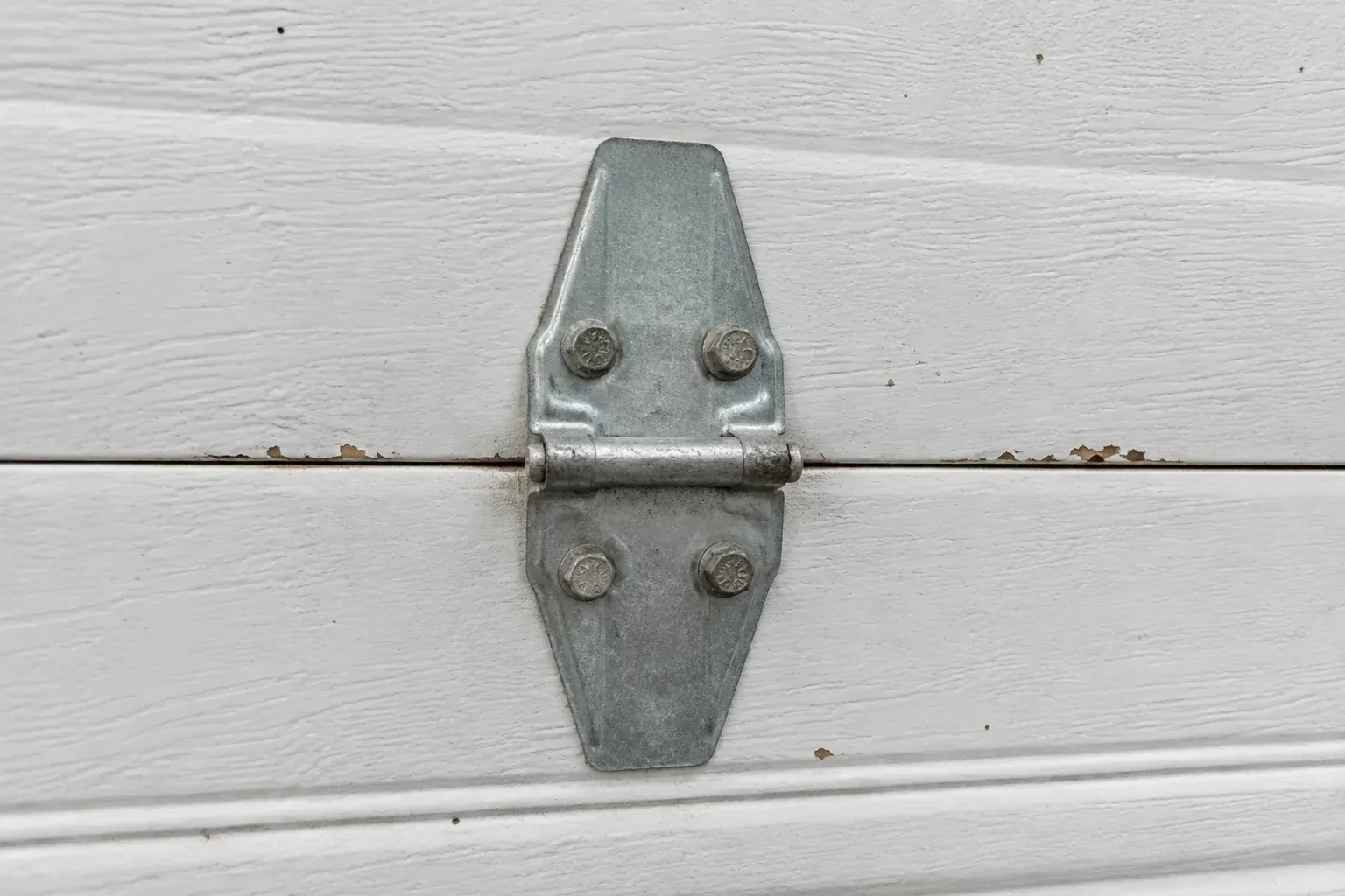 Metal center hinge across a seam in a white sectional garage door. — Garage Door Hinge Replacement, Toronto